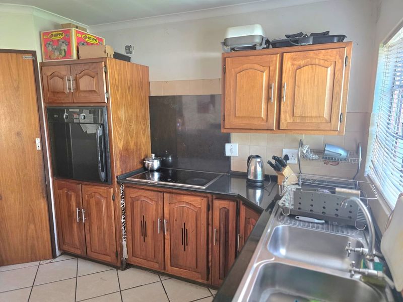 A functional kitchen featuring wooden cabinetry, a built-in oven, electric hob, and a double sink with tiled flooring and backsplash.