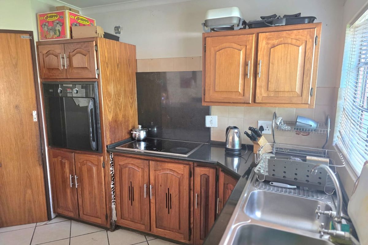 A functional kitchen featuring wooden cabinetry, a built-in oven, electric hob, and a double sink with tiled flooring and backsplash.