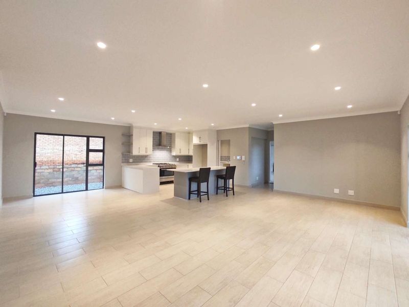 Spacious open-plan living area featuring a modern kitchen with a central island, gas stove, and sleek tiled flooring, leading to an outdoor space.
