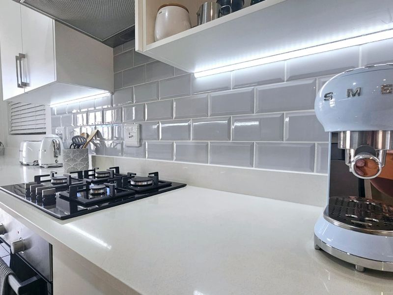 Modern kitchen featuring a sleek gas cooktop, built-in oven, subway tile backsplash, and quartz countertops with integrated under-cabinet lighting.