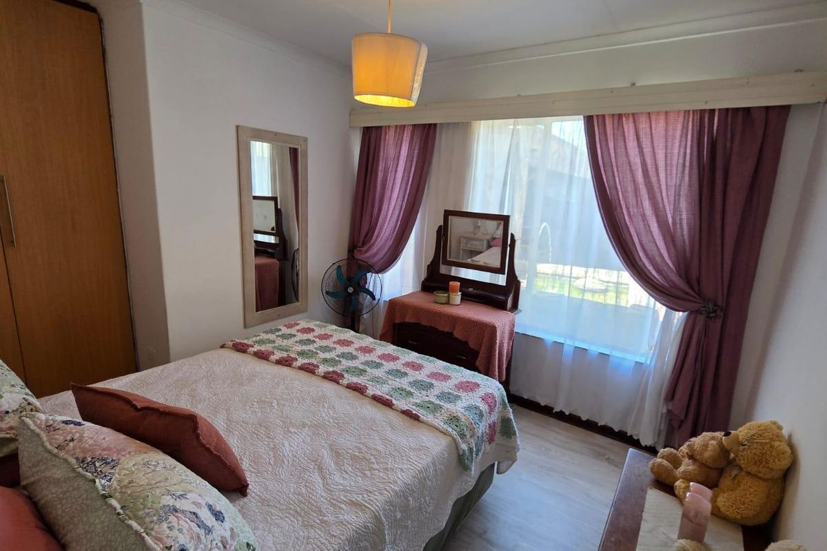 A cozy bedroom featuring built-in wooden cabinetry, light-toned flooring, and a large window with curtains allowing natural light into the space.