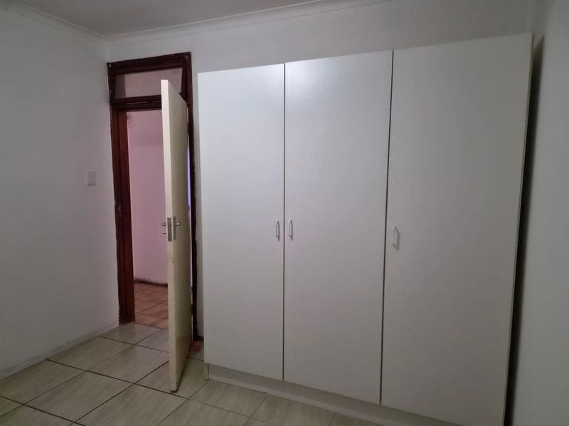 A bedroom featuring neutral tiled flooring and a large, white built-in wardrobe with ample storage space.