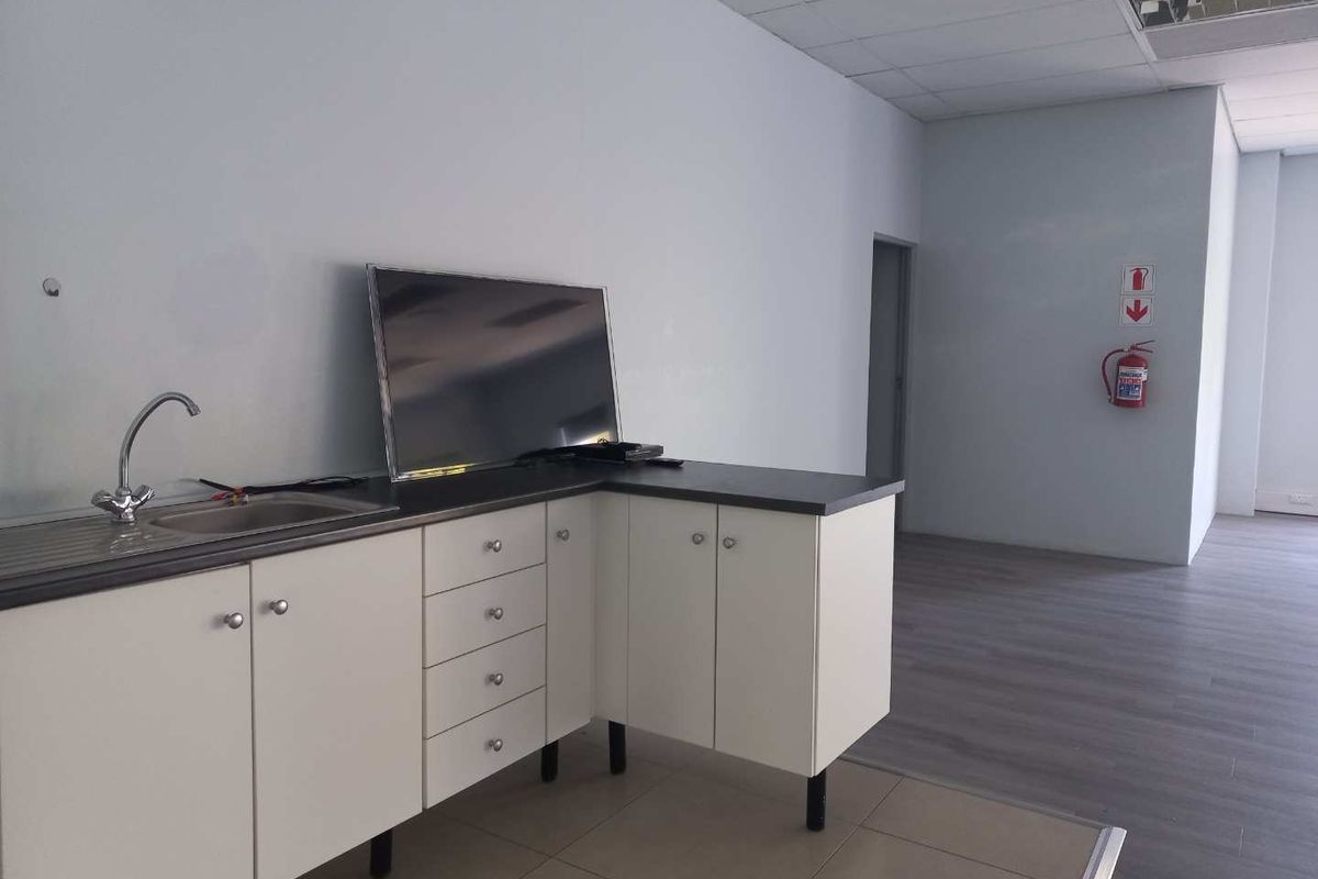 A functional office kitchenette area featuring white cabinetry, a stainless steel sink, and laminate flooring, with a fire extinguisher mounted on the wall.
