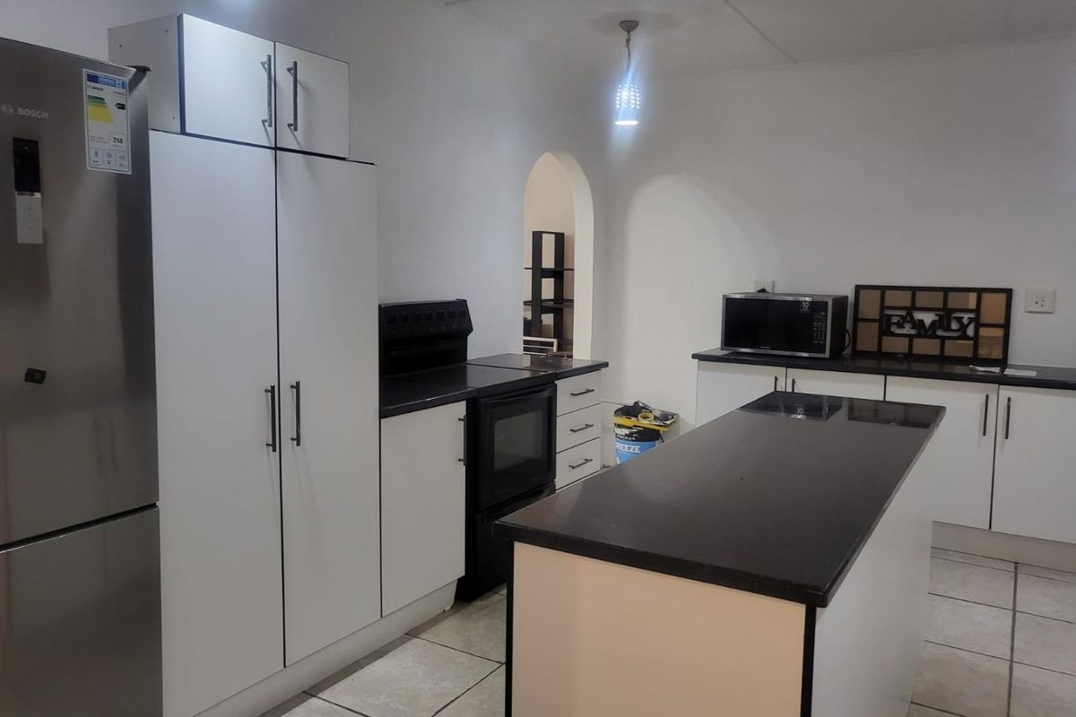 A functional kitchen featuring white cabinetry, dark stone countertops, a central island, and ceramic floor tiles, providing a clean and practical workspace.