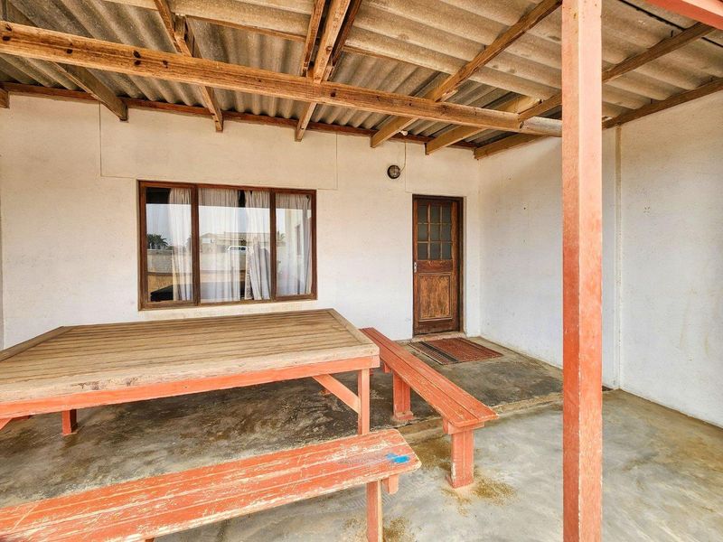 A covered outdoor patio area featuring a corrugated roof, timber support beams, and direct access to the home via a timber door.