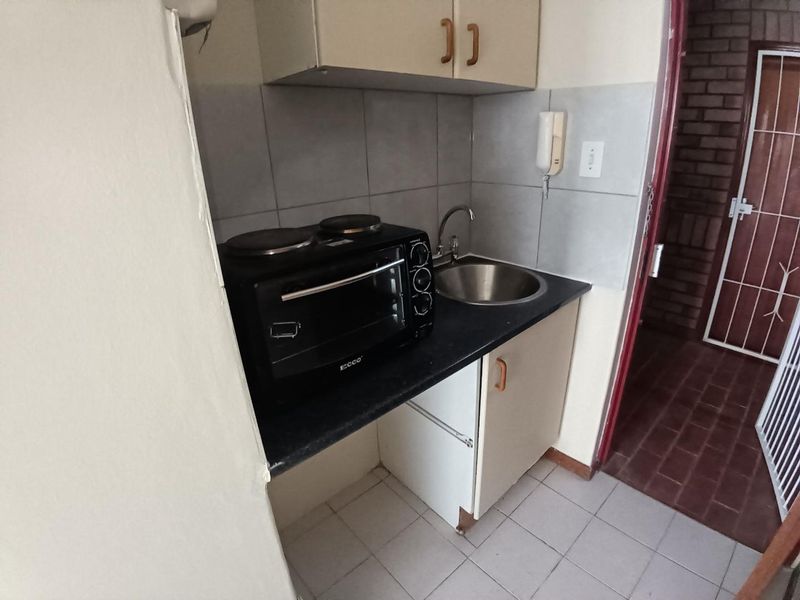 Compact kitchen area featuring built-in cabinetry, a stainless steel sink, tiled backsplash, and tiled flooring, providing a functional space for basic meal preparation.