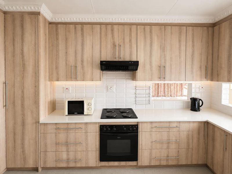 Modern kitchen featuring light wood-grain cabinetry, white subway tile backsplash, quartz countertops, and integrated black appliances with elegant crown molding.