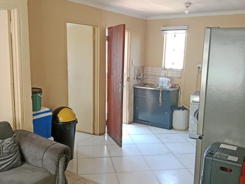 Open plan living area featuring tiled flooring and a compact kitchen corner with a sink unit and tiled splashback.