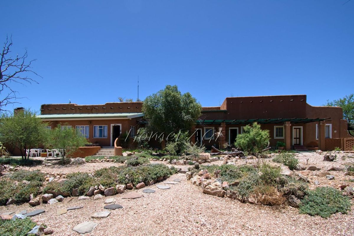 A view of the rear exterior of the farm property, featuring a traditional adobe-style facade, covered patio area, and landscaped desert garden.