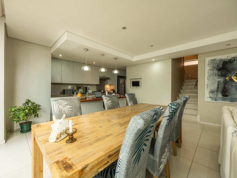 Open-plan dining and kitchen area featuring tiled floors, modern cabinetry, granite countertops, and a staircase leading to the upper level.