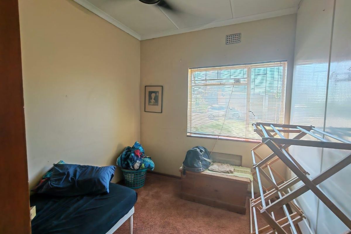 A compact bedroom featuring carpeted flooring, a ceiling fan, and a window with fitted blinds.