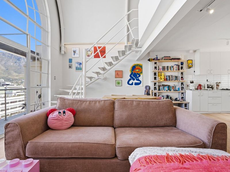 Bright open-plan living area featuring a modern kitchen, striking arched window with mountain views, and a contemporary staircase leading to an upper level.