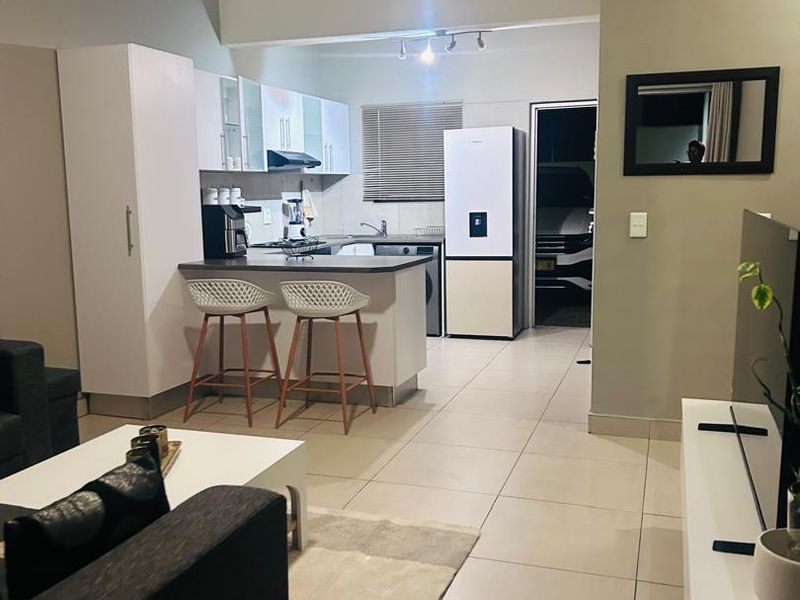 Open plan living area featuring a modern kitchen with built-in cabinetry, breakfast counter, and tiled flooring throughout.