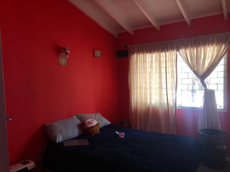 A bedroom featuring exposed timber ceiling beams and security bars on the window, currently finished with bold red wall paint.