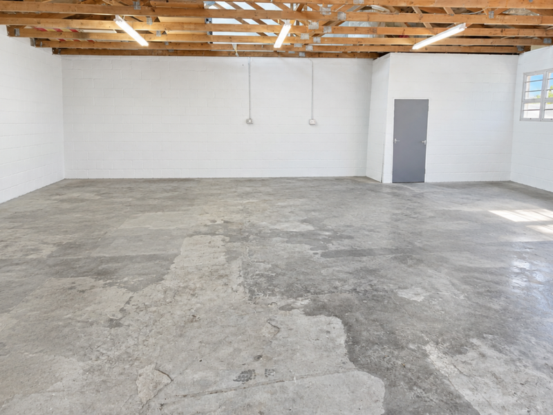 Spacious industrial utility area featuring exposed timber roof trusses, concrete flooring, and painted block walls, suitable for storage or workshop use.
