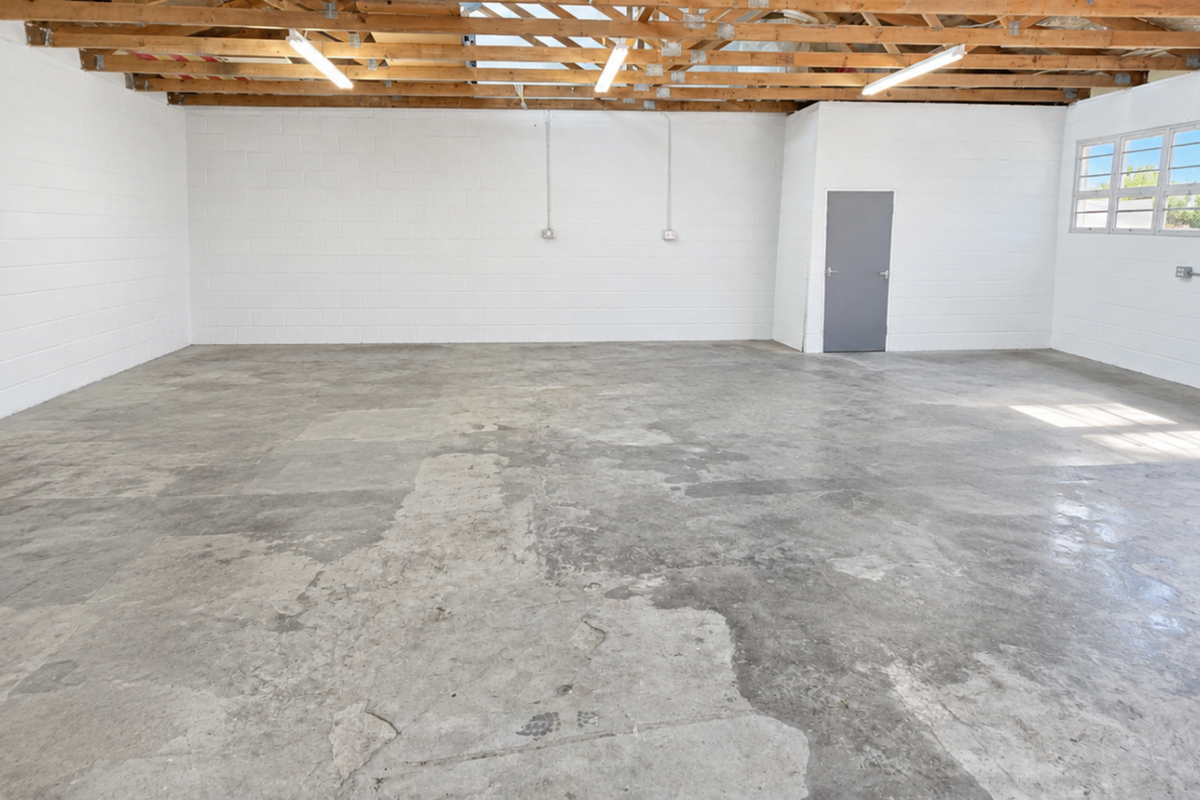 Spacious industrial utility area featuring exposed timber roof trusses, concrete flooring, and painted block walls, suitable for storage or workshop use.