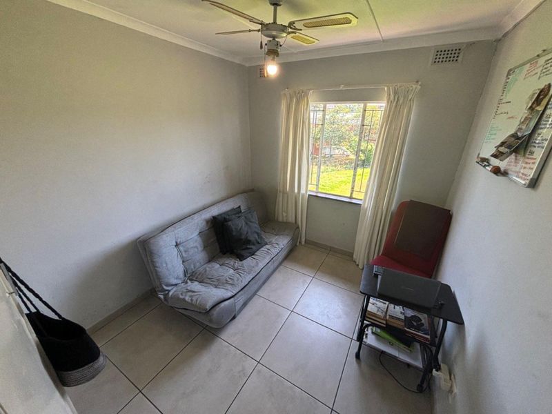 A compact bedroom featuring tiled flooring, a ceiling fan, and a window with natural light, offering a functional space for rest or study.