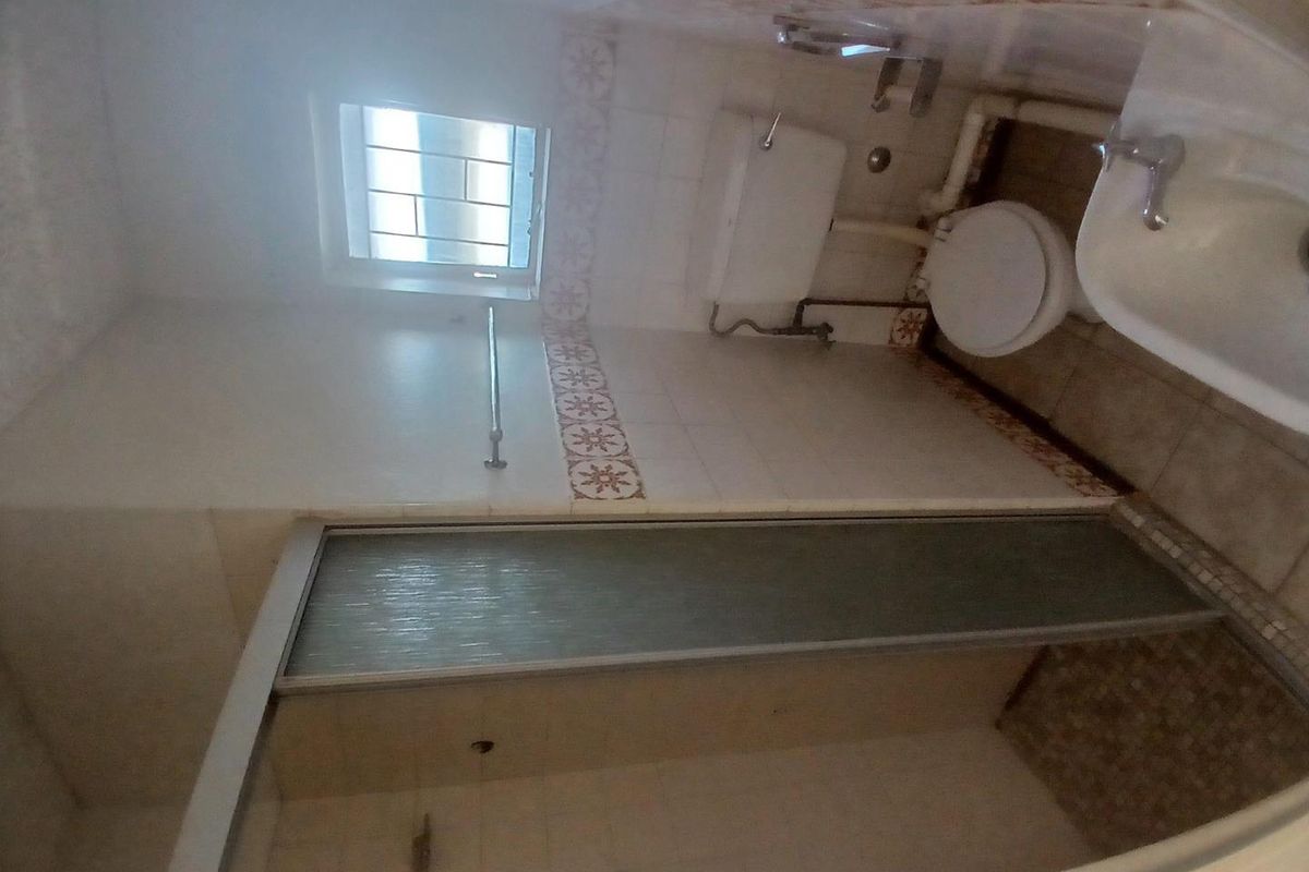 A dated bathroom featuring a shower enclosure, toilet, and washbasin with tiled finishes and exposed plumbing.