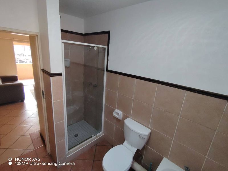 A dated bathroom featuring a shower enclosure, toilet, and tiled finishes, requiring cosmetic updates to improve its overall condition and appeal.
