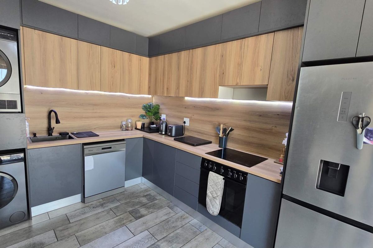 Modern kitchen featuring two-tone cabinetry, wood-look countertops, integrated oven, hob, and built-in laundry appliances for a sleek, functional workspace.