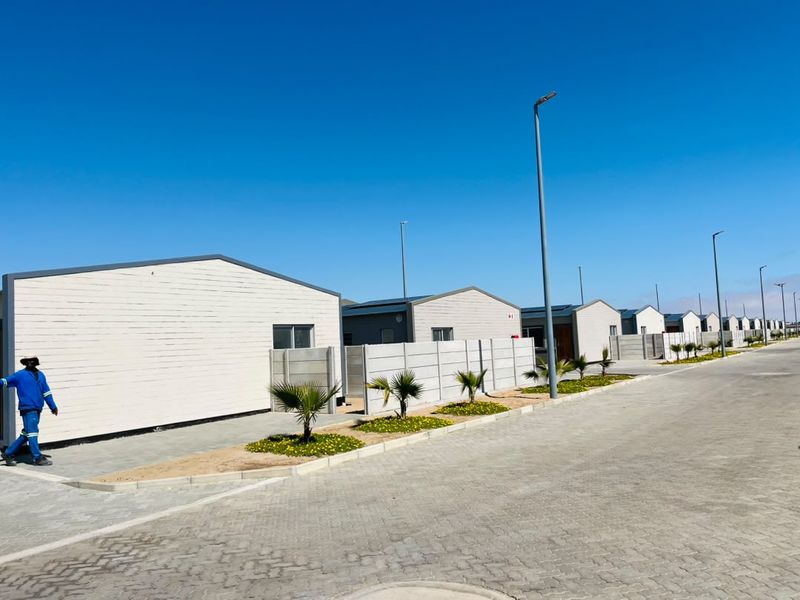 A street-level view of a modern townhouse development featuring uniform architectural design, paved driveways, and precast concrete boundary walls.