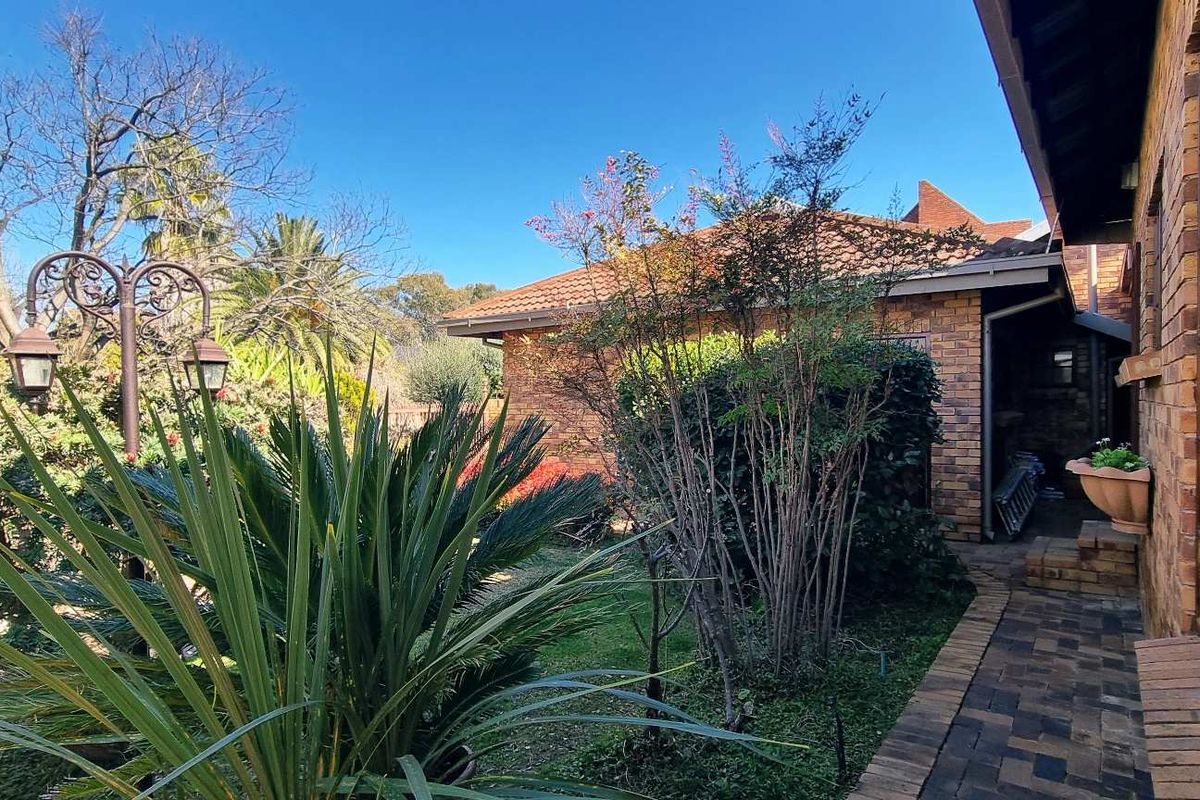 A view of the rear exterior of the house, featuring a brick facade, paved walkway, and established garden area.