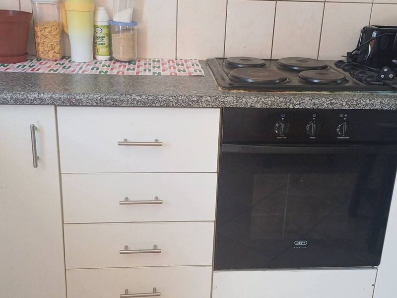 A functional kitchen area featuring white cabinetry, a granite-look laminate countertop, a built-in oven, and an electric hob with a tiled backsplash.