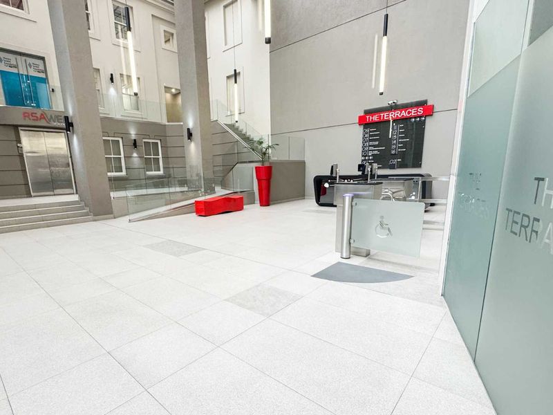 Modern office building entrance lobby featuring high ceilings, tiled flooring, security turnstiles, and clear directory signage for The Terraces.