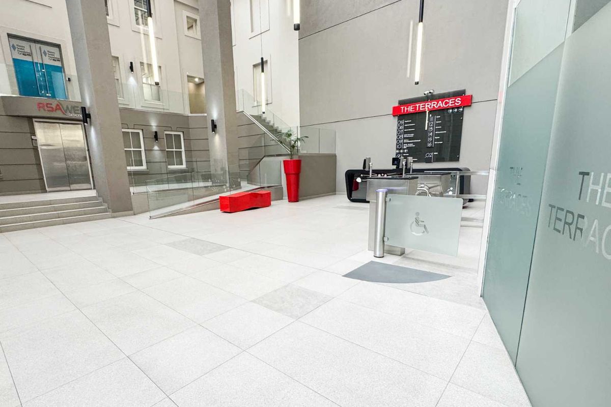 Modern office building entrance lobby featuring high ceilings, tiled flooring, security turnstiles, and clear directory signage for The Terraces.