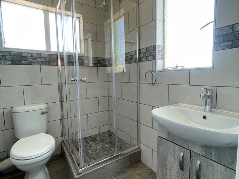 A clean, modern bathroom featuring a glass shower enclosure, a vanity cabinet with a basin, and neutral wall and floor tiling.