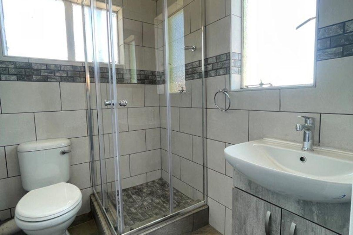 A clean, modern bathroom featuring a glass shower enclosure, a vanity cabinet with a basin, and neutral wall and floor tiling.