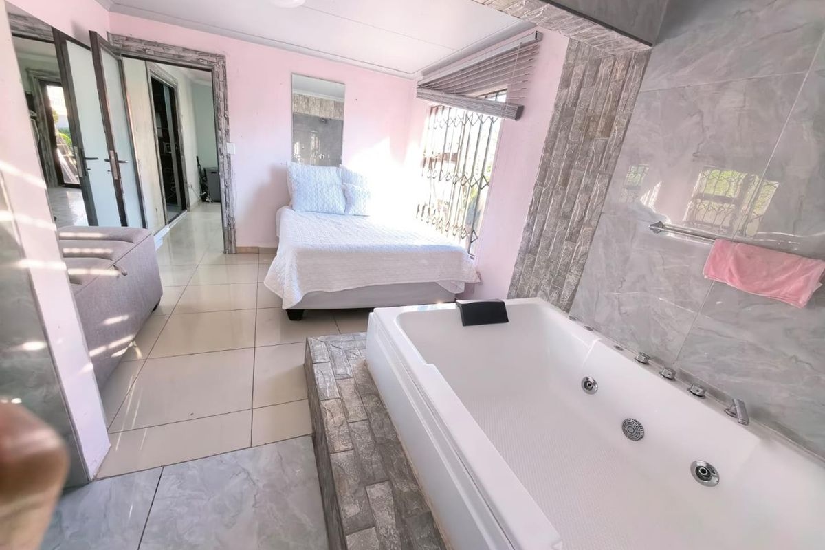 A spacious bedroom featuring an integrated spa bath, stone-cladding accents, tiled flooring, and direct access to the hallway.