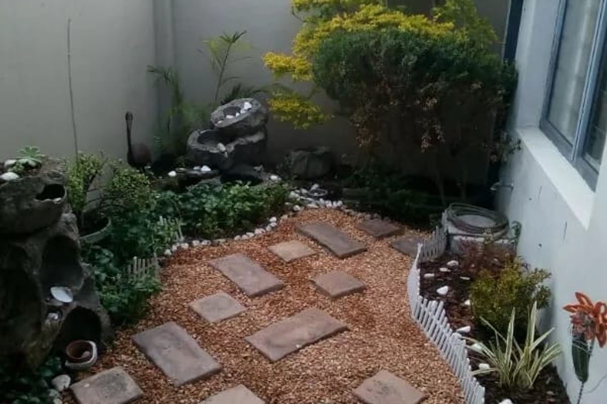 A compact, landscaped rear courtyard featuring gravel ground cover, stone pavers, perimeter walling, and established garden beds.