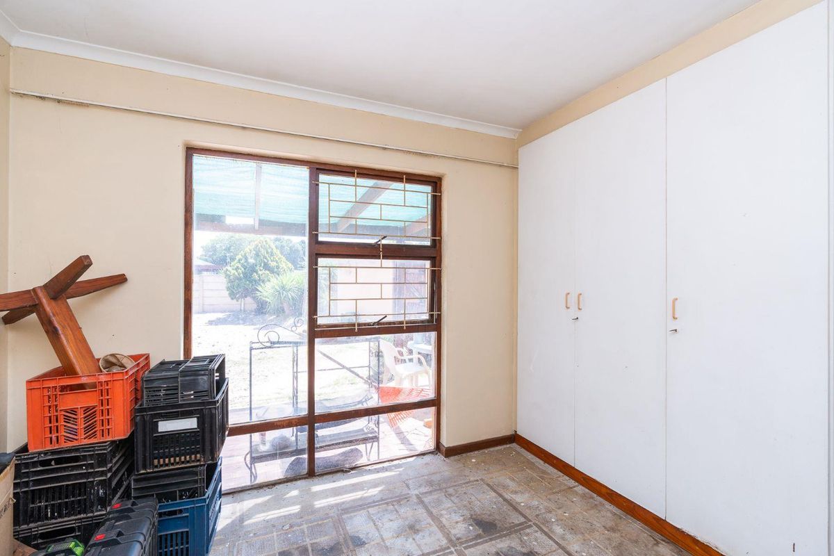 A bedroom featuring built-in cupboards, a large window with security bars, and worn flooring, offering a blank canvas for renovation.