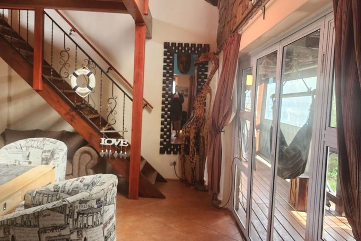Spacious living area featuring exposed timber beams, a feature brick wall, ceramic tiled flooring, and large sliding doors leading to an outdoor deck.