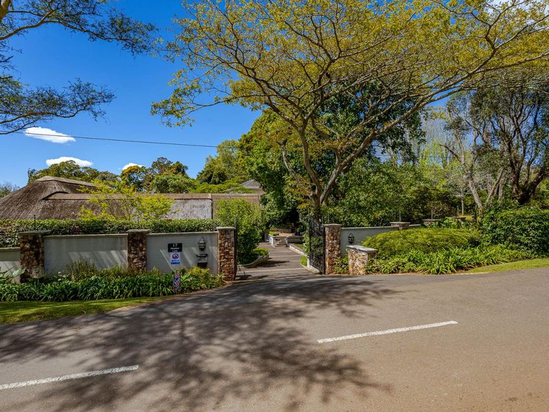 A well-maintained front entrance featuring a stone-clad boundary wall, wrought iron gate, and a glimpse of a traditional thatched roof property.