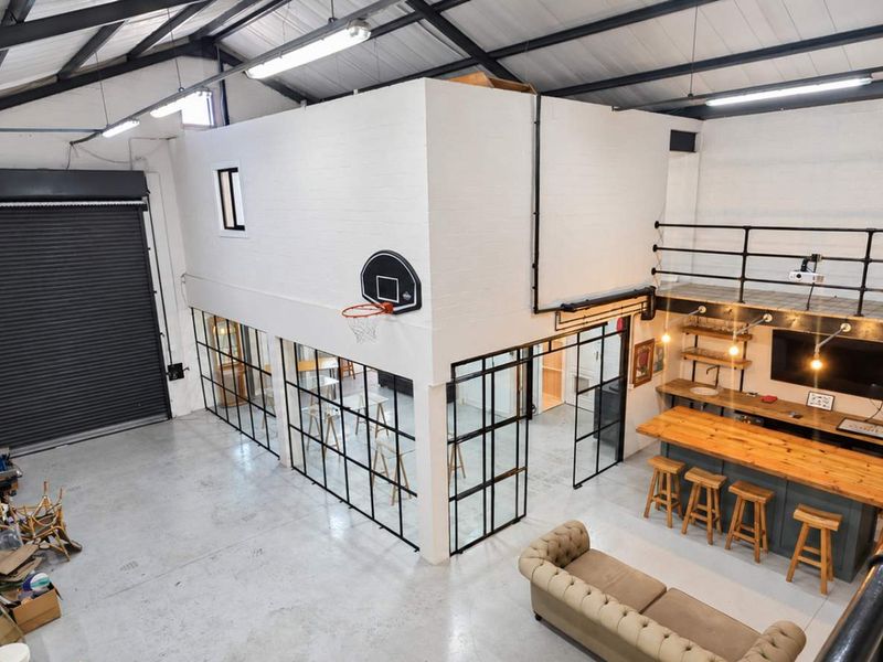 Spacious industrial open-plan area featuring high ceilings with exposed steel trusses, a mezzanine level, polished concrete floors, and modern black steel-framed glass partitions.