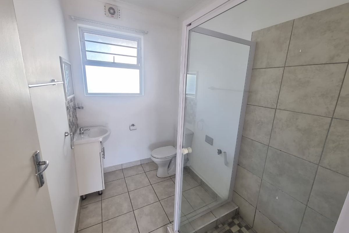 A functional bathroom featuring a glass-enclosed shower, vanity basin, and toilet with neutral tiled finishes.