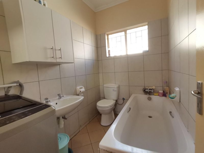 Functional bathroom featuring a bathtub, pedestal basin, and toilet, with full-height wall tiling and overhead storage cabinetry.