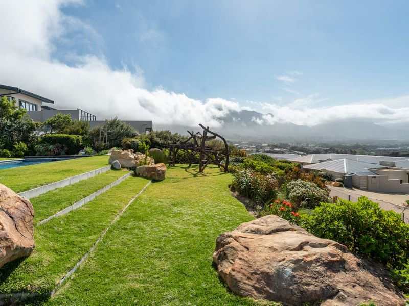 A beautifully landscaped garden featuring tiered lawn areas, large decorative boulders, and a swimming pool with expansive mountain and valley views.
