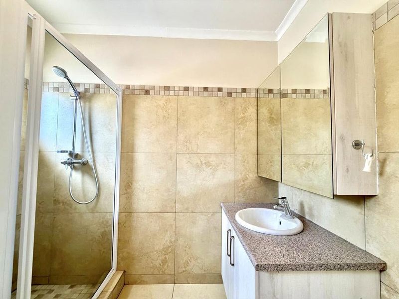 A clean, functional bathroom featuring a glass-enclosed shower, a vanity with a built-in washbasin, and neutral wall tiling.