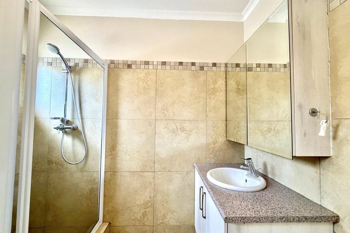 A clean, functional bathroom featuring a glass-enclosed shower, a vanity with a built-in washbasin, and neutral wall tiling.