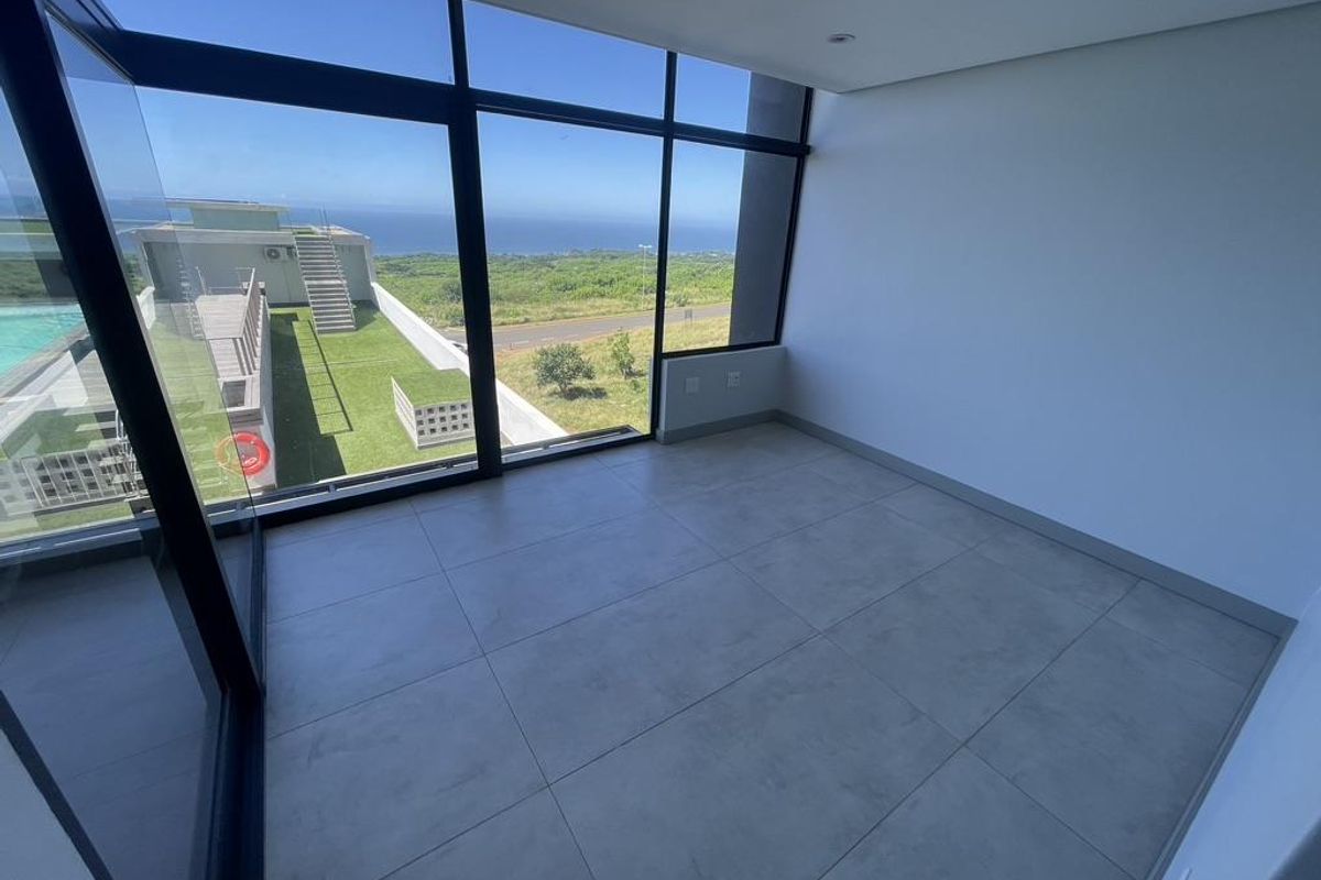A bright, empty room featuring large floor-to-ceiling windows with expansive coastal and landscape views, finished with modern neutral floor tiles.