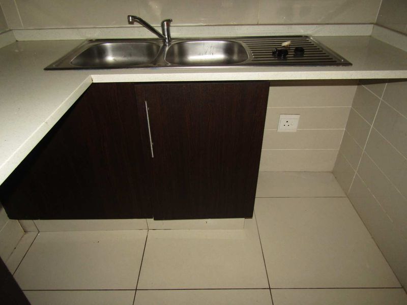 A functional kitchen area featuring dark wood cabinetry, a stainless steel double sink with a mixer tap, and neutral tiled finishes.