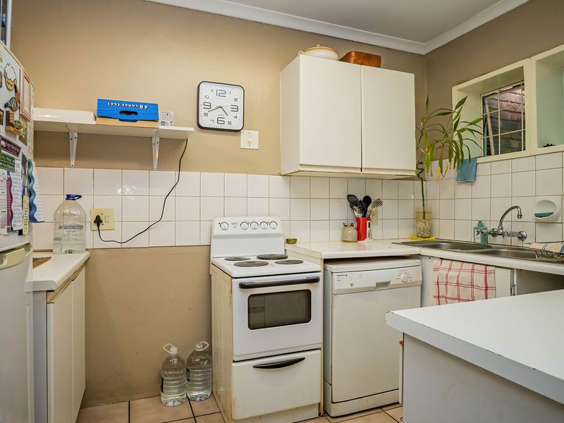 A functional kitchen featuring built-in cabinetry, an electric stove, and a double sink with tiled splashbacks, offering potential for modernization.