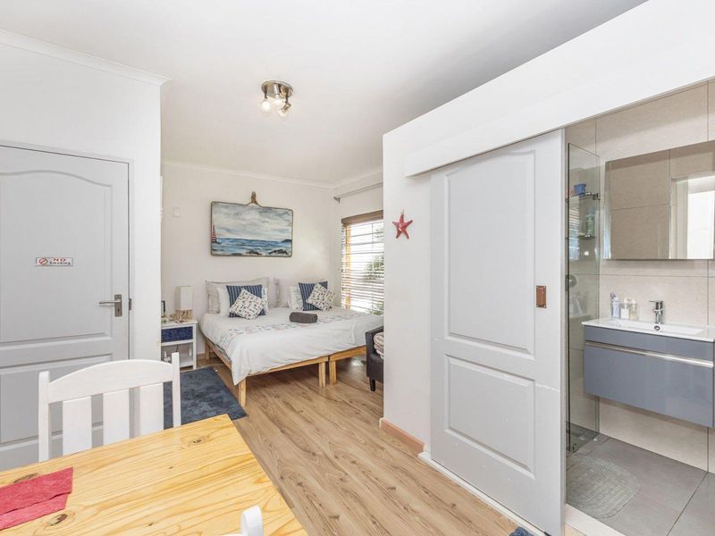 A well-maintained bedroom featuring laminate flooring, a sliding door leading to an en-suite bathroom with a modern vanity and glass shower enclosure.