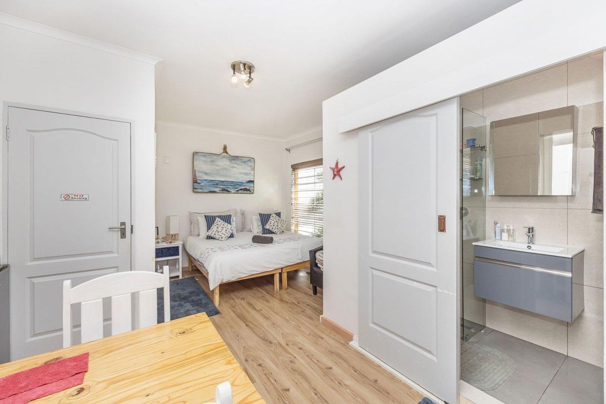 A well-maintained bedroom featuring laminate flooring, a sliding door leading to an en-suite bathroom with a modern vanity and glass shower enclosure.