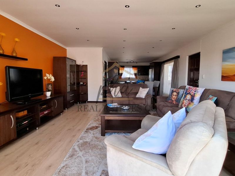 Spacious open-plan living area featuring laminate flooring, recessed downlighting, and a bright accent wall, flowing seamlessly into the kitchen space.