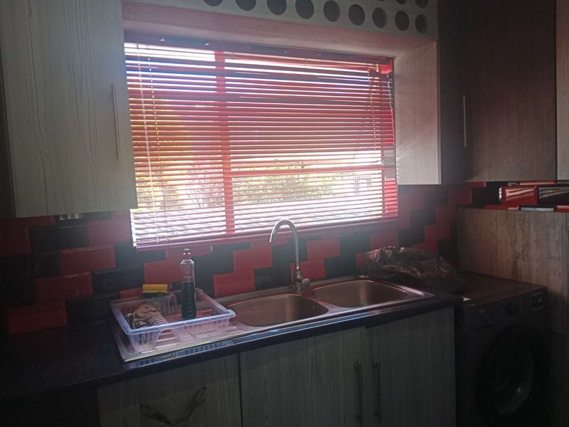 A functional kitchen area featuring a double bowl stainless steel sink, gooseneck tap, and contrasting tiled splashback with built-in cabinetry.