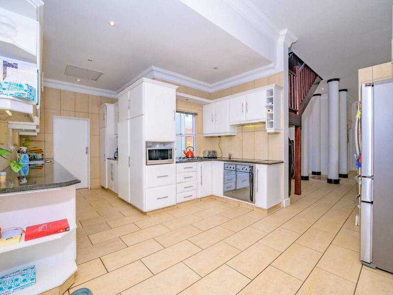 Spacious kitchen featuring white cabinetry, granite countertops, built-in appliances, and tiled flooring, seamlessly flowing into an open-plan area with a staircase and decorative columns.
